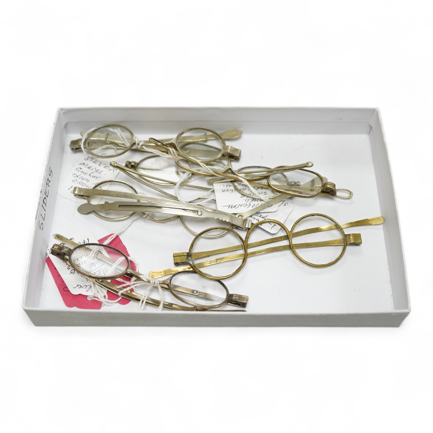 Three pairs of early 19th century base metal slider spectacles, pseudo hallmarks, one also stamped Pebbles, and two pairs of similar temple spectacles, the pair with turn pin sides also stamped pebbles, the pair with obl